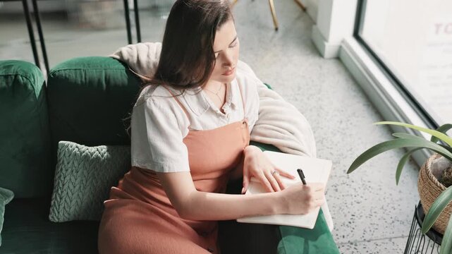 Woman, writing and home with journal in living room for planning schedule or checklist. Above book, creative and thinking of female freelancer for remote work, copywriting or ideas for article editor