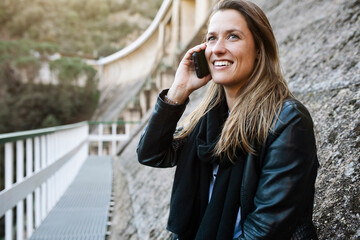 Trendy young woman talking phone with smartphone outdoors at dam during autumn, winter. Technology concept. 