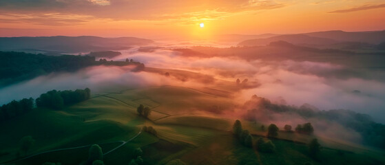 Fototapeta premium Aerial view of breathtaking sunrise over misty landscape with rolling hills and verdant fields
