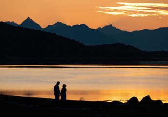 Romantic couple silhouette next to beautiful colorful evening sky during the midnight sun in...