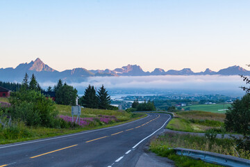 Road leading to Leknes during the midnight sun in Lofoten, Northern Norway. Beautiful mountain landscape with peak raging above the clouds and mist