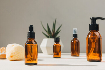 Set of natural cosmetics. Amber bottles with facial, bath liquid on a concrete background with natural bath sponge. Front view