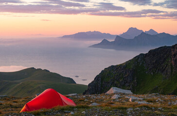 Camping with a tent over a colorful sea of clouds during the midnight sun in Lofoten