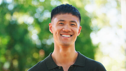 Young Man Smiling Outdoors at a Park on a Sunny Day Surrounded by Greenery