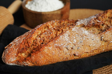 Fresh bread on a black napkin next to a bowl of flour and a wooden rolling pin on a dark background