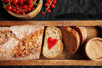 Fresh sliced ​​bread with a heart of berry jam on a wooden tray next to a bowl of red currants...