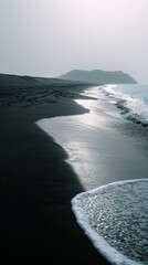 Deserted black sand beach with gentle waves and mountain in the background.