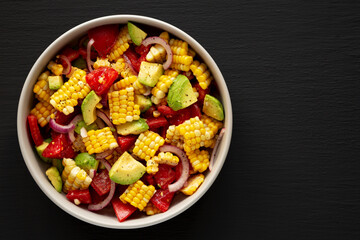Healthy Fresh Corn Salad in a Bowl on a black background, top view. Flat lay, overhead, from above. Copy space.