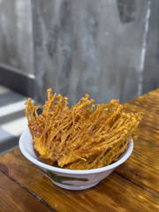 Spicy and crispy enoki mushrooms in white bowl on wooden table.