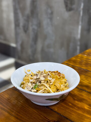 Pad Thai noodles in white bowl on wooden table.