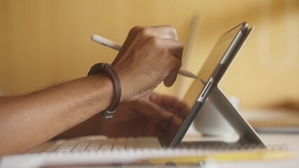Close up detail of creative black man drawing with pen in tablet at desk.  