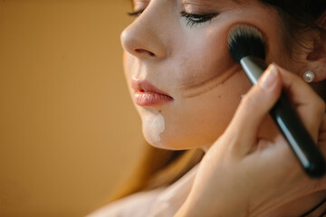 A close-up of a make-up artist applies make-up to a young model girl before a photo shoot.