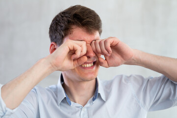Man scretching itchy eyes on gray background