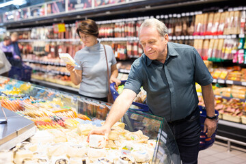 Older man picking out fresh cheese to buy in grocery store