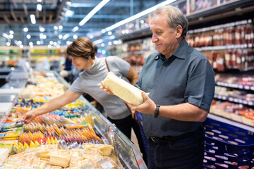 Elderly male customer looking around in dairy section of supermarket