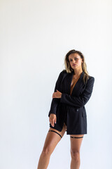 Fototapeta premium A beautiful blonde poses on a white background in a photo studio in a black jacket and panties. Full length photo