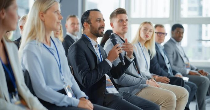 Multiethnic Male Technology Conference Attendee Sittign In Crowd And Using Microphone To Ask A Question Related To Presentation Of An Innovative Gadget. Middle Eastern Man At International Tech Forum.