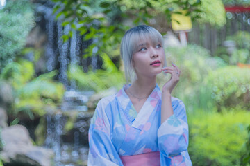 Pretty girl in a Yukata dress.  Portrait fashion young Asian women wearing a traditional Japanese kimono or Yukata dress and holding pink umbrella are happy and relaxing in the fresh green nature.