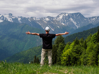 A man with outstretched arms against the background of majestic mountains, personifying freedom, joy and unity with nature