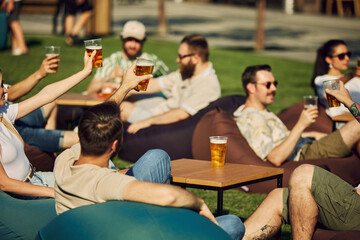 Sunny Celebration. Group of friends, gathering for a picnic, sharing laugh and engaging conversation while clinking beer glasses. Concept of summer, leisure, friendship, meeting, fun, relaxation