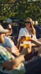 Cheers. Young smiling men and women,friends celebration, having party outdoors on warm summer day, cheerfully talking and drinking beer. Concept of summer, leisure, friendship, meeting, relaxation