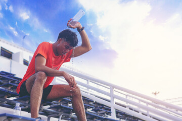 Tired runner man with a bottle of water pouring to himself for freshness after training outdoor...