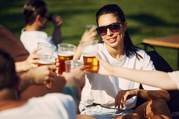 Joyful gathering. Group of friends, men and women sitting outdoors in restaurant, talking, laughing and drinking refreshing beer. Concept of summer, leisure, friendship, meeting, fun, relaxation