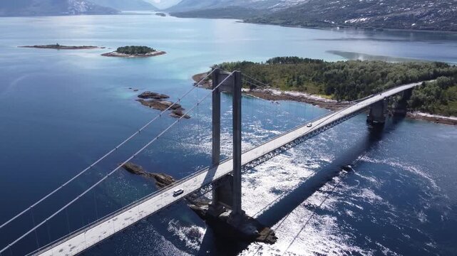 Aerial drone view of bridge in Northen Norway with cars driving on top and sharp mountains in the background