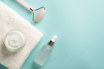 Skin care products. Cream jar, jade roller and serum bottle on blue background.