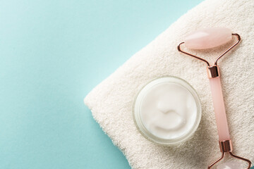Skin care products. Cream jar, jade roller and white towel on blue background. Flat lay with copy space.