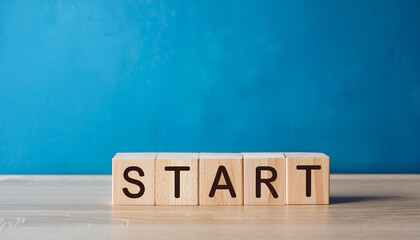 Wooden cubes with word START on table with bright blue backdrop wall.