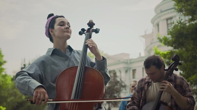 Group of young talented performers playing music instruments while busking in park on sunny day