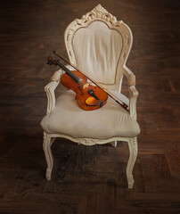 wooden violin lies on armchair old vintage style, classic furniture royal throne chair white fabric upholstery dark gothic fantasy room background. Musical instrument without people filming object 4k © kharchenkoirina