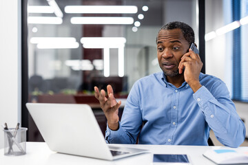 Mature African American office worker engaged in phone conversation at workplace. Professional in...
