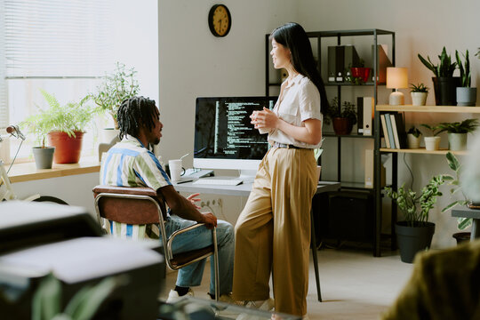 Joyful young ethnically diverse male and female colleagues chatting during coffee break at work in modern IT company office