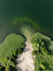 Aerial drone view of summer lake beach. People sunbatching on the lake beach.Sunny summer holiday at the green lake. Sunbathing  and rest on the beach. Holiday on the lake in Poland.