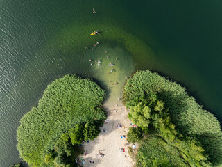 Aerial drone view of summer lake beach. People sunbatching on the lake beach.Sunny summer holiday at the green lake. Sunbathing  and rest on the beach. Holiday on the lake in Poland.