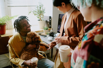 Cheerful young Black man introducing his lovely dog to female colleagues at working in modern pet-friendly office