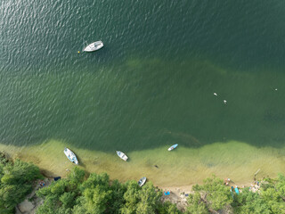 Aerial drone view of summer lake beach. Boats on the shore of a beautiful lake. Sunny summer holiday at the green lake. Holiday on the lake in Poland.