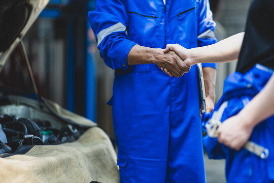 Car service. Mechanic and customer shaking hands. Excellent cooperation between car mechanic and coworker. Close up mechanic and maintenance engineer shaking hands at car workshop.