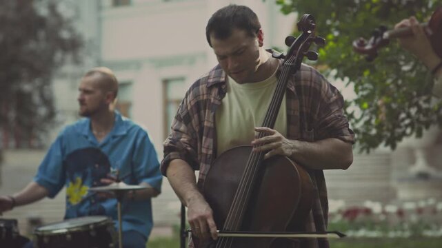 Young ensemble practicing playing classic music instruments such as violin, cello and drums while having rehearsal outdoors in park