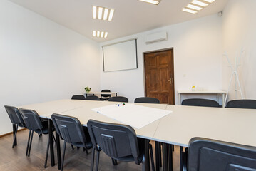 Conference room with benches, tables and a projector. Empty Conference Room In Modern Office. Interior of a classroom with white walls and wooden floor.  Office Business.