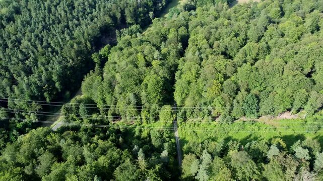 Drohne fliegt an Hochspannungsfreileitung, Schneise durch den Wald, Luftaufnahme