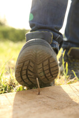 Careless worker stepping on nail in wooden plank outdoors, closeup