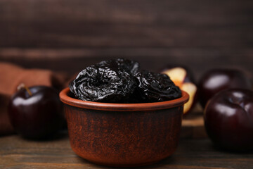 Tasty dried plums (prunes) in bowl on wooden table, closeup