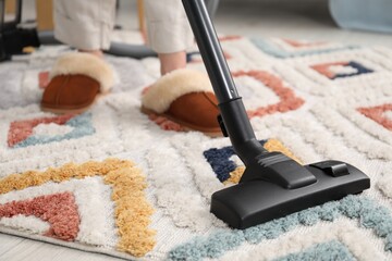 Woman cleaning carpet with vacuum indoors, closeup
