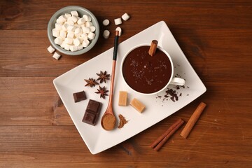 Tasty melted chocolate in cup, marshmallows, candies and spices on wooden table, flat lay