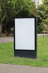 Blank advertising vertical street billboard poster in a green park mockup template. Empty white city light poster mock up template.