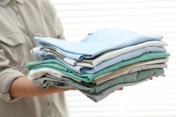 Woman with stack of clean clothes indoors, closeup