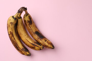 Bunch of ripe bananas with dark spots on pink background, top view. Space for text